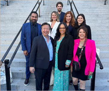 A diverse group of people posing together in business professional attire in front of stairs at the White House.
