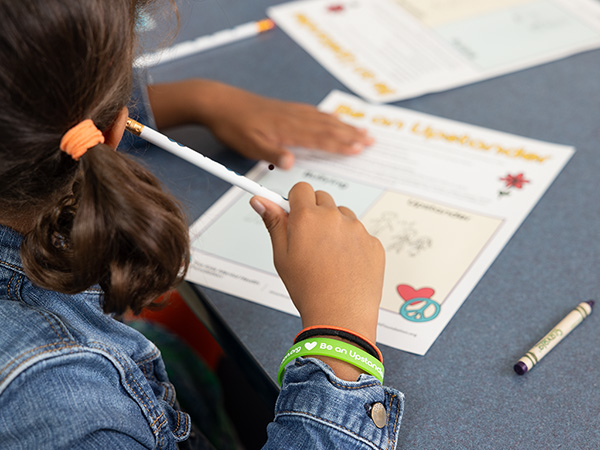 Student participates in a 'Day Time Break' classroom activity from Kids Mental Health Foundation, wearing a green 'Be an Upstander' wristband and holding a pencil thoughtfully.