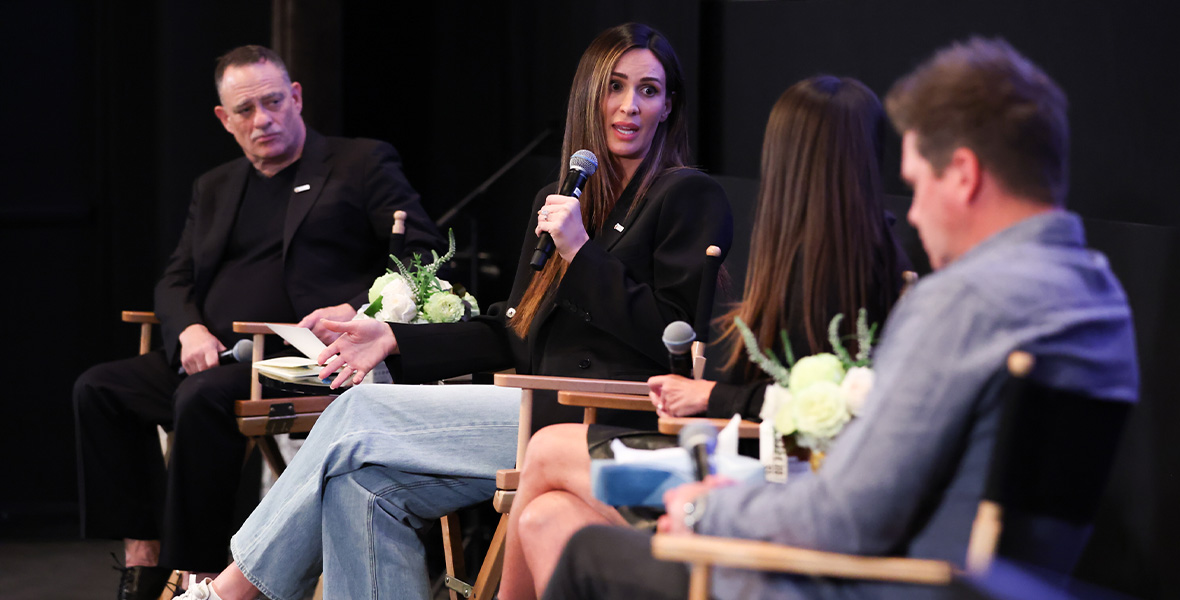 Angel Carter Conrad speaks on a mental health awareness panel, holding a microphone and seated among fellow advocates and experts, highlighting the importance of open conversations around grief, healing, and youth support.