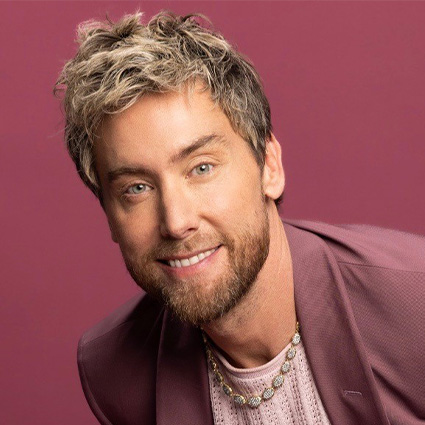 Headshot of Lance Bass wearing a light pink sweater and mauve blazer, smiling in front of a rose-colored background. The singer and mental health advocate supports youth emotional wellness initiatives.