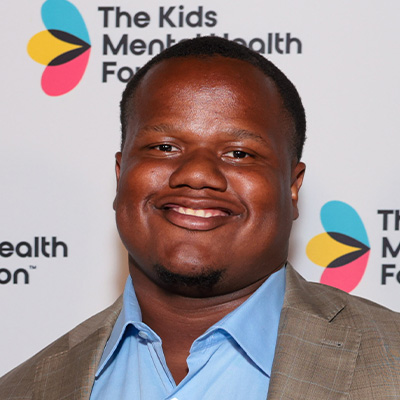 Tyler Davis smiles for a headshot in front of a branded The Kids Mental Health Foundation backdrop.