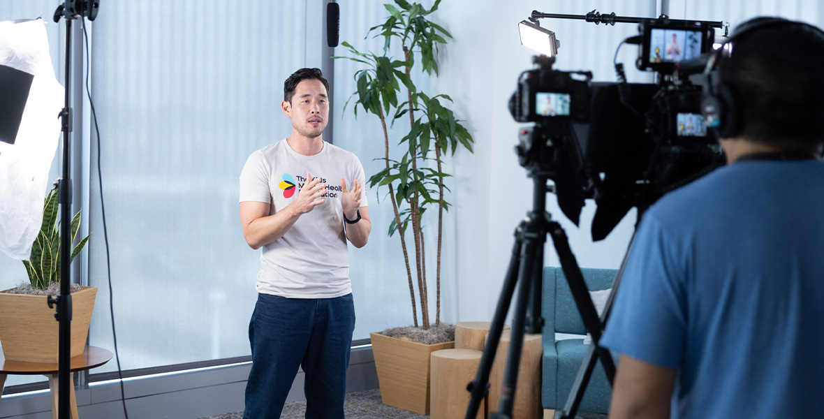 Actor Raymond Lee volunteers at a Kids Mental Health Foundation event, smiling alongside a child and staff members at a colorful activity table honoring first responders and family support.
