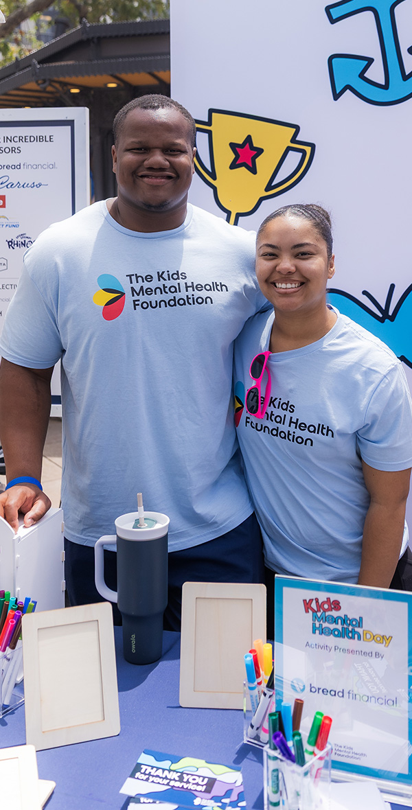 Tyler Davis and a Kids Mental Health Foundation team member smile at a Kids Mental Health Day activity table featuring mental health resources and activities.