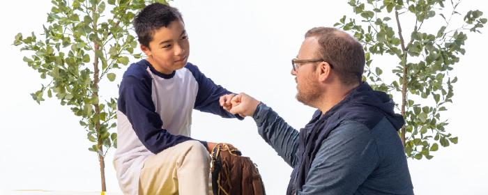 Adult mentor and young boy share a fist bump while sitting outdoors, symbolizing trust, support, and positive adult-child relationships in youth mental health programs.