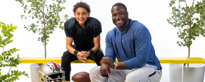Young football player and coach smile together on a bench with a football, representing mentorship and partnerships that support youth mental health through sports.