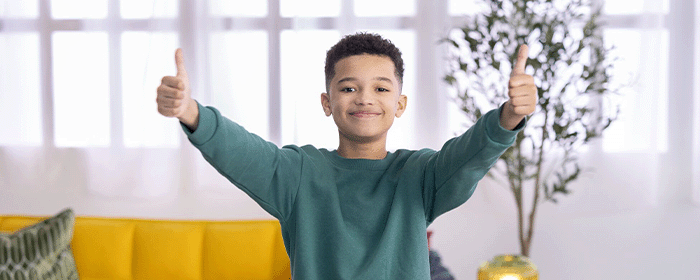Smiling boy in a green sweatshirt gives two thumbs up, symbolizing confidence, positivity, and emotional wellness supported by Kids Mental Health Foundation resources.