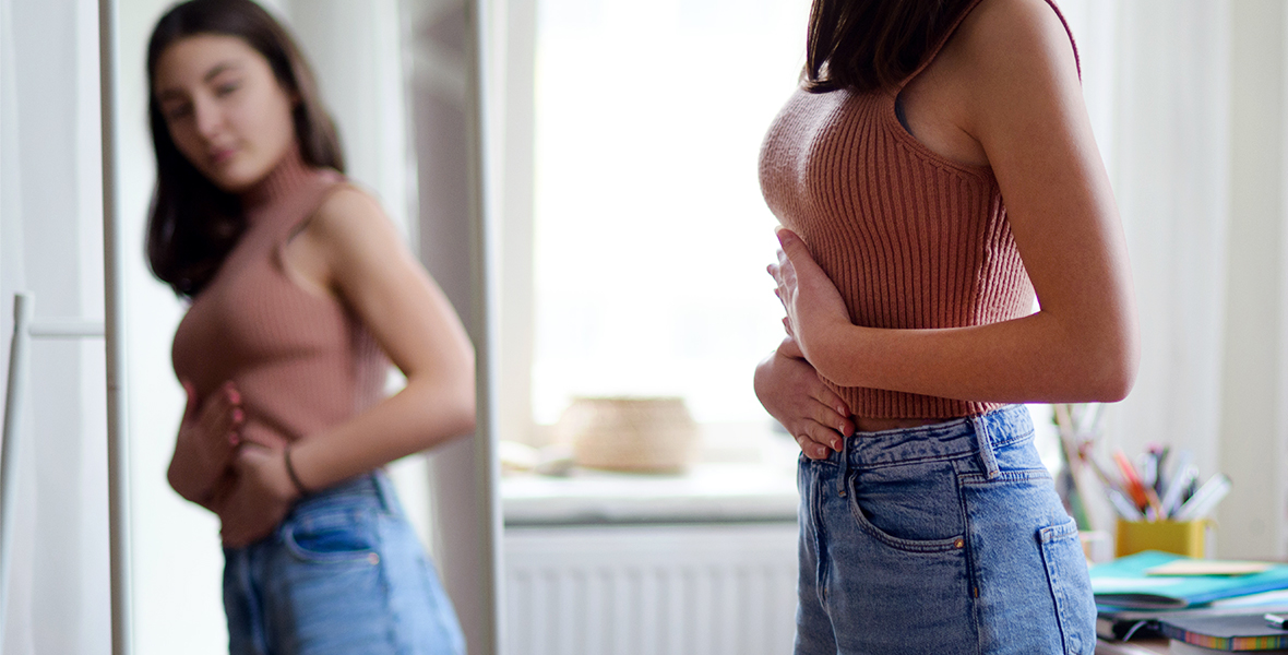 Teen girl examining her body in the mirror, struggling with body image and self-esteem. Raising awareness about body positivity, self-acceptance, and mental health in youth.
