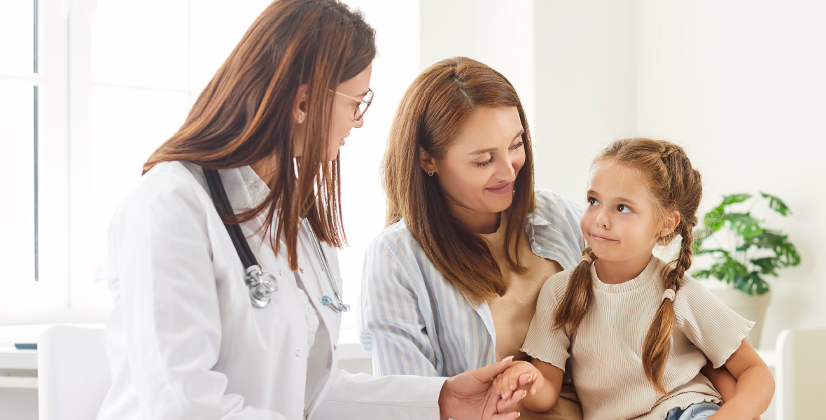 Pediatrician speaks with a mother and young child during a checkup, creating a supportive environment for discussing child development, including autism and emotional well-being.
