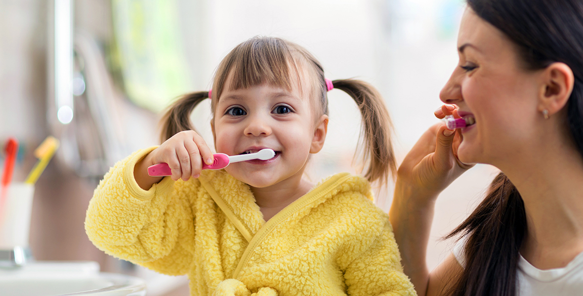 A happy young girl brushing her teeth with her mother, promoting healthy routines and self-care for children's mental wellness. Bright and cheerful morning routine fostering positive habits and bonding.