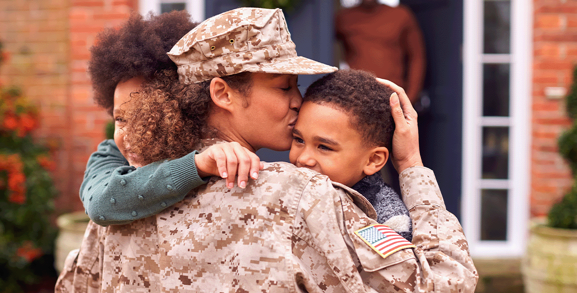 Military parent in uniform embraces and kisses her two young children during a heartfelt reunion at home, symbolizing family connection, resilience, and support for military families.