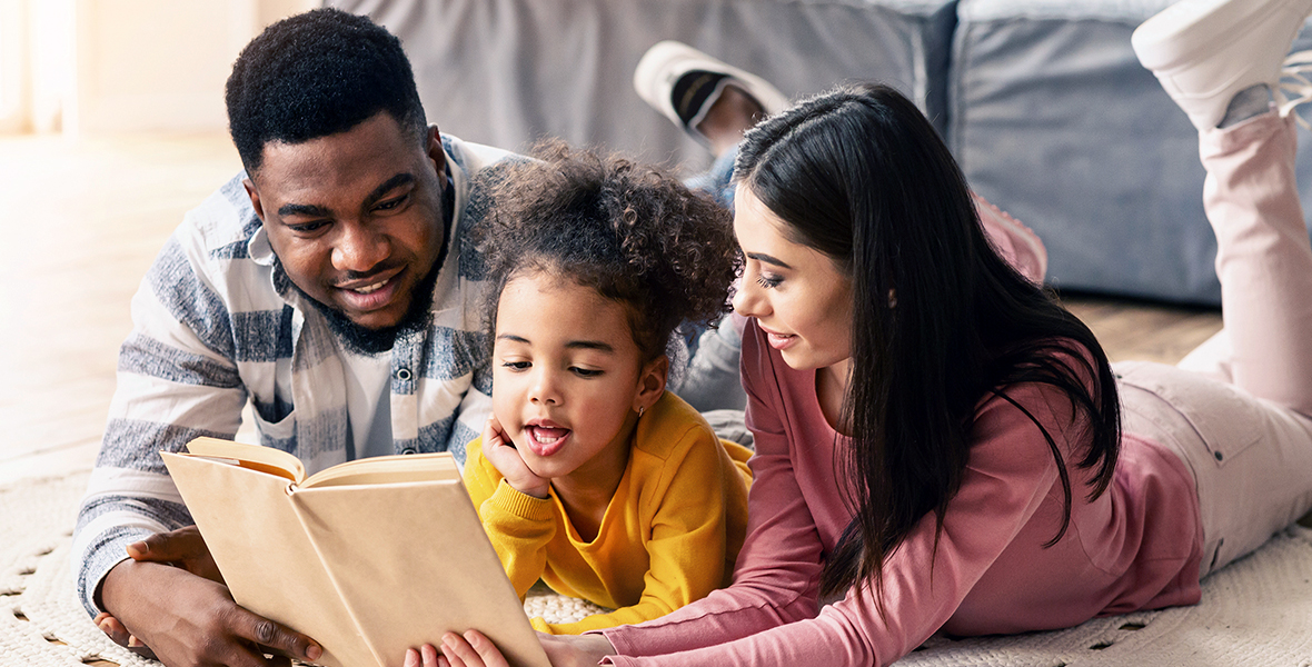 Happy multiracial family reading together at home, fostering emotional connection and early childhood development. Supportive parenting and literacy for children's mental health and well-being.