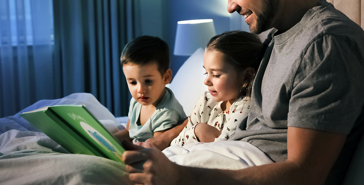 Father reading a bedtime story to his young children, creating a comforting nighttime routine that supports emotional bonding and children's mental well-being.