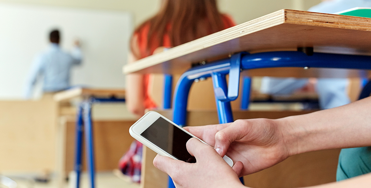 Student using a smartphone in class instead of paying attention to the teacher. The impact of technology and social media on education, focus, and mental health in youth.