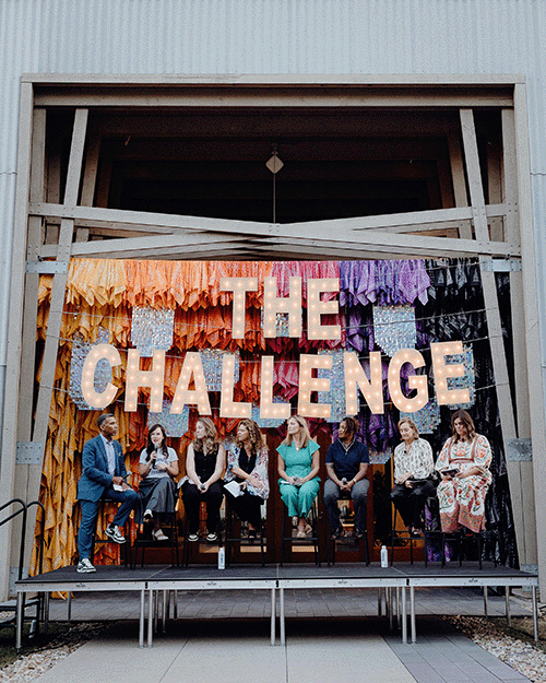 Panelists seated on a stage beneath a large illuminated "The Challenge" sign during a Kids Mental Health Foundation event, with colorful hanging decorations in the background.