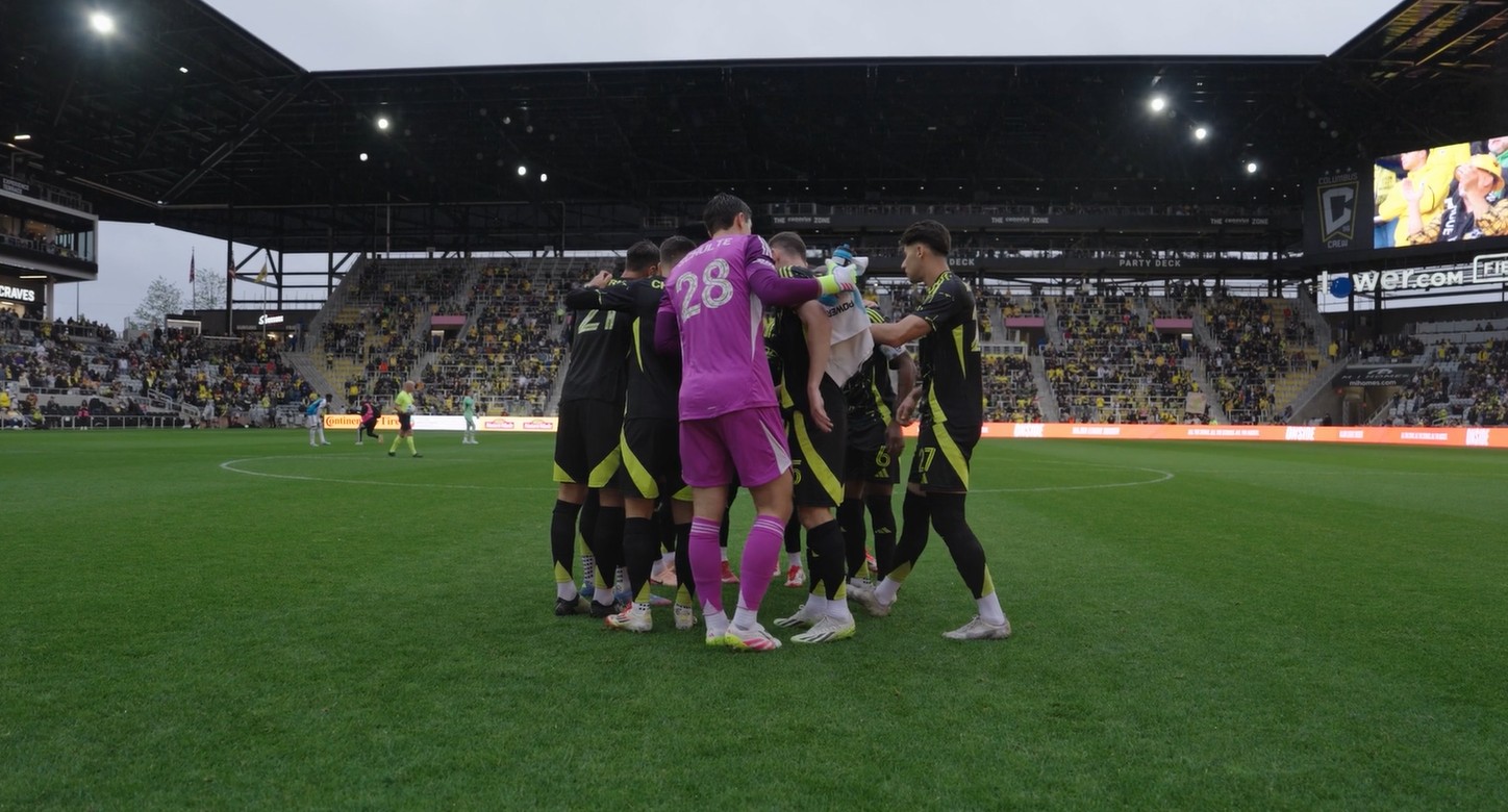 Columbus Crew soccer players in black uniforms before a match at ScottsMiracle-Gro Field, facing a packed stadium during pre-game ceremonies.