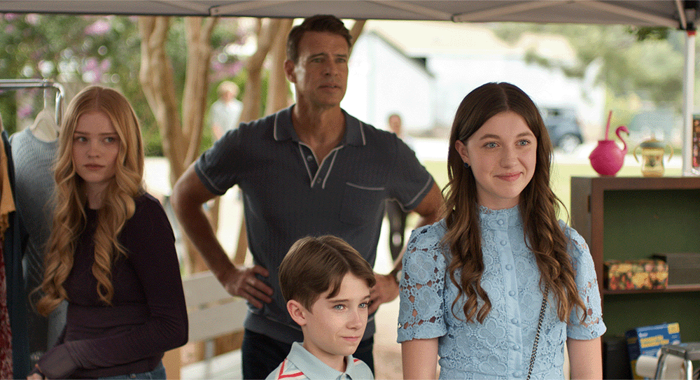 Family shopping together at an outdoor market in a scene from “It’s Not Like That,” featuring parents and children interacting during a community outing