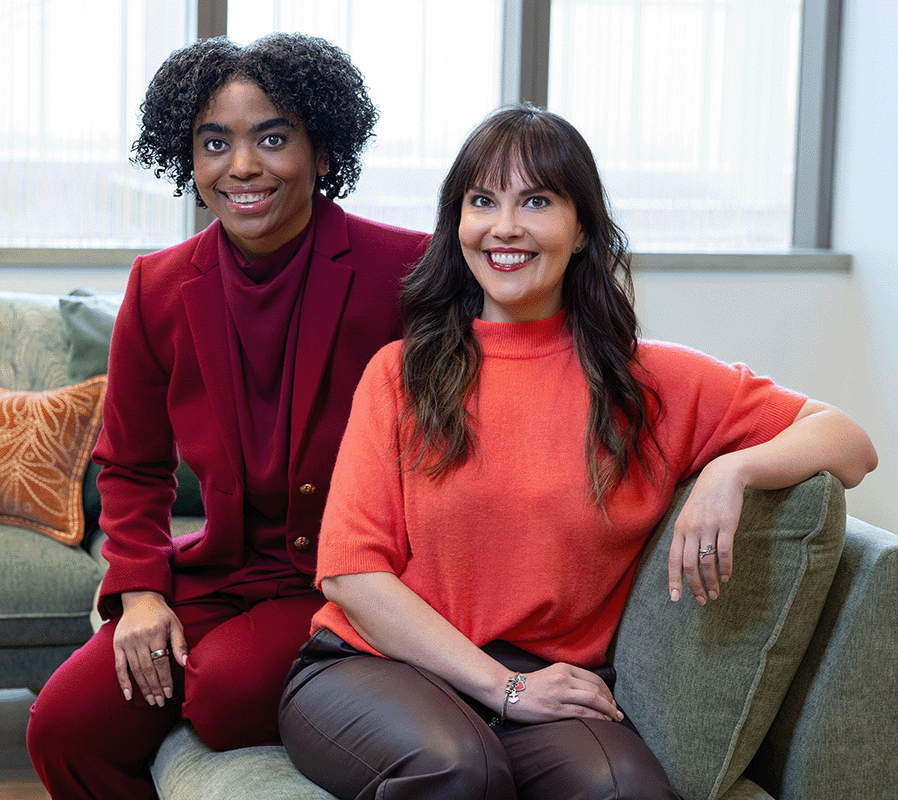 Dr. Ariana Hoet and Dr. Whitney Raglin Bignall sit together smiling in a professional setting, representing leadership and expertise in children’s mental health at The Kids Mental Health Foundation.