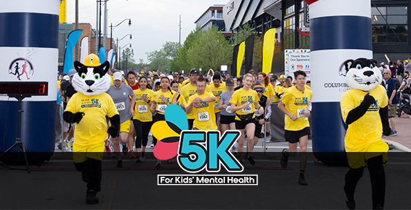 Runners in yellow shirts kick off a mental health awareness 5K, led by two mascots at the starting line, promoting wellness and community support.