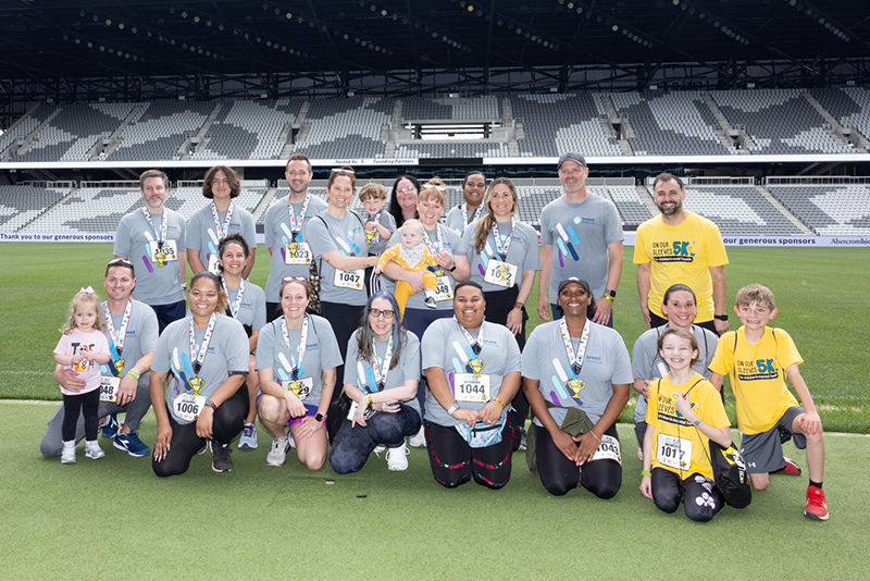 A diverse group of participants, wearing medals, pose on a stadium field after completing a mental health awareness 5K, celebrating community and support.