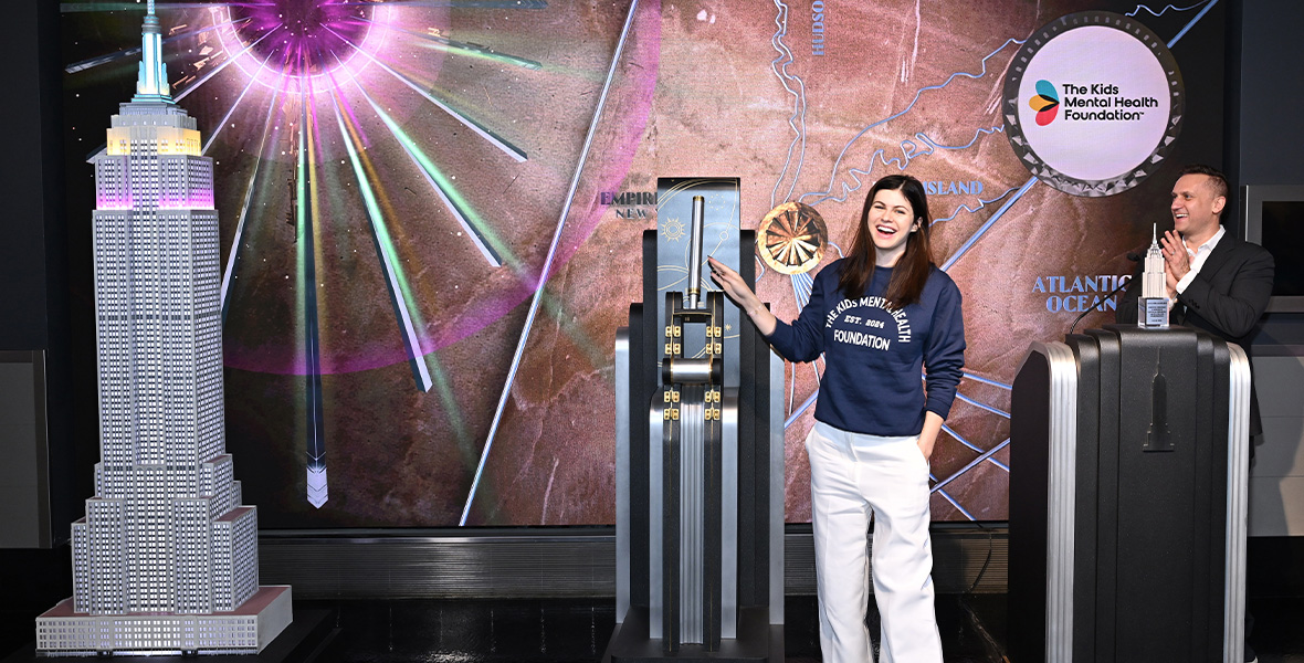 La actriz Alexandra Daddario ilumina el Empire State Building en homenaje a la Fundación para la Salud Mental Infantil, vestida con la sudadera de la fundación y sonriendo durante el acto de sensibilización.