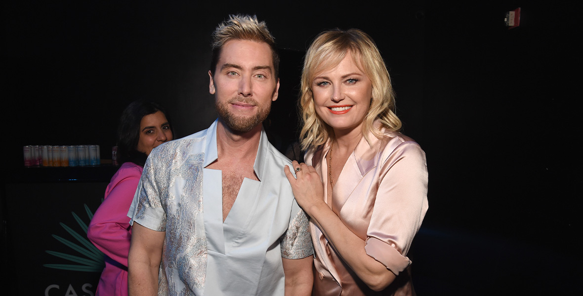 Lance Bass y Malin Åkerman posan juntos en un evento de la Fundación para la Salud Mental Infantil, sonriendo y mostrando su apoyo al bienestar mental de los jóvenes en un ambiente nocturno.