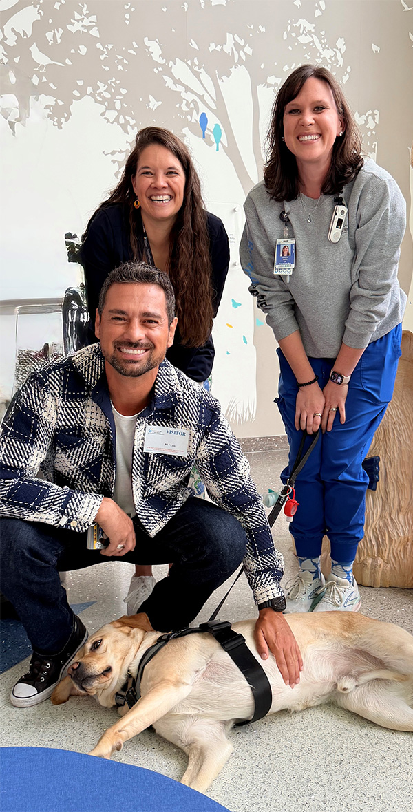 El actor J.R. Ramírez visita el Nationwide Children’s Hospital y posa con miembros del personal y un perro de terapia durante un acto de participación comunitaria.