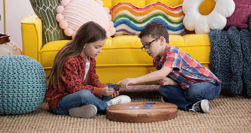 Dos niños jugando juntos a un juego de cartas en casa, lo que ilustra una interacción social positiva y formas saludables de practicar la paciencia, la cooperación y el control emocional.
