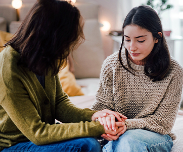 Un adulto toma con delicadeza de la mano a una adolescente triste durante una conversación sincera, lo que simboliza el apoyo emocional y aborda los sentimientos de tristeza o desesperanza entre los jóvenes.
